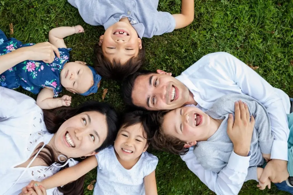 Family laughs and giggles in the grass for a sweet, silly moment.