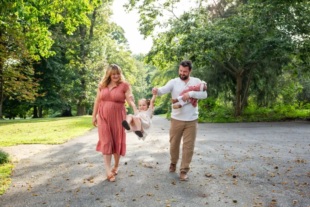 Little girls swings between her parents as the family enjoys a peaceful evening walk.