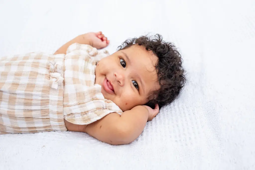 Curly-haired baby girls smiles and her eyes sparkle.