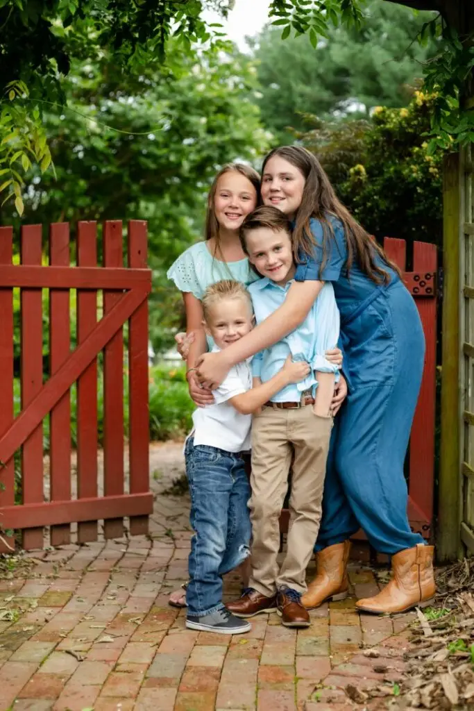 Sisters and brothers hug by a gate on their family farm.