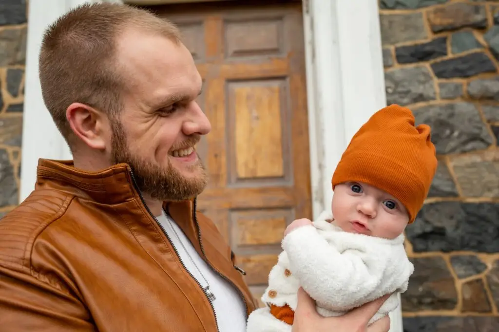 Blue-eyed baby boy gazes forward while Dad smiles over him.